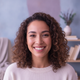 Headshot of a smiling woman in her late 20s, with a blurred background of soft blue and lilac tones.