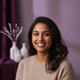 Headshot of a smiling South Asian woman in her late 20s, wearing casual attire, against a soft, blurred background.